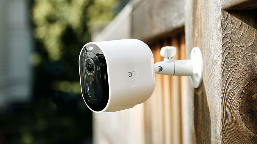 cámara de vigilancia exterior Arlo blanca y negra colocada en la valla de madera
