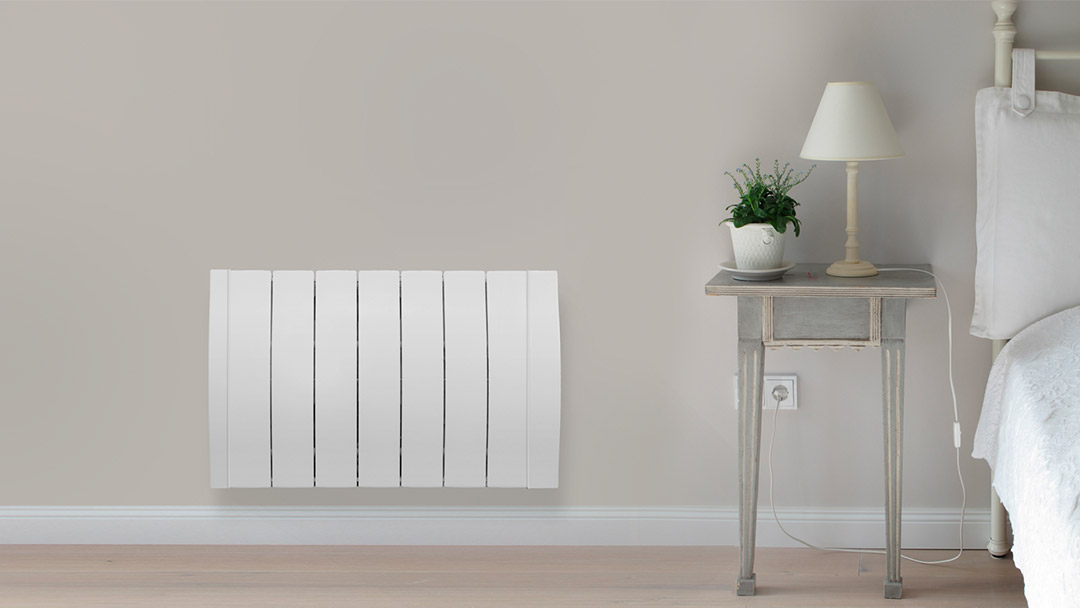 Uno de los radiadores eléctricos de color blanco en el dormitorio al lado de la mesita de noche