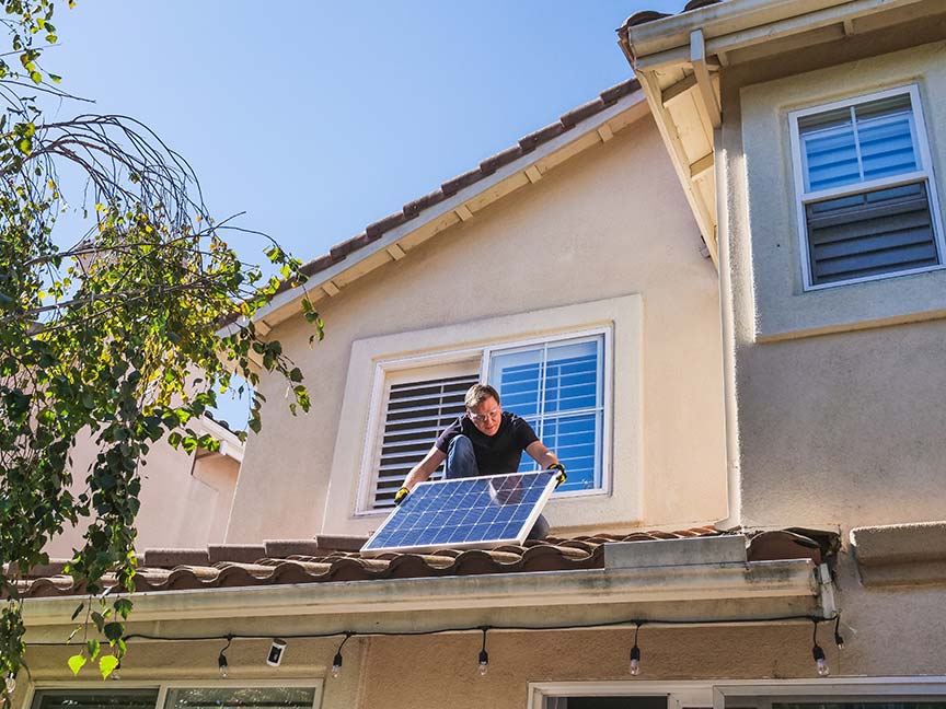 Hombre colocando una placa solar sobre el tejado de una vivienda unifamiliar