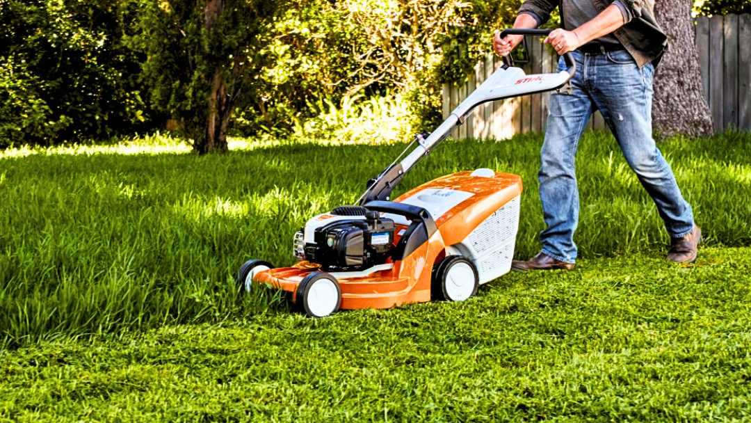 hombre manejando una de las cortacésped gasolina de color naranja en el jardín